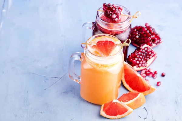 Jars with pomegranate and grapefruit juice on blue background. Refreshments and summer drinks. — Stock Photo, Image