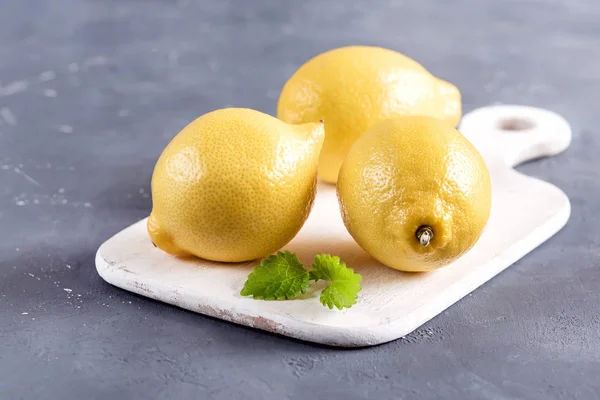 회색 배경에 노란색 신선한 감귤 류의 민트 잎 절단 보드에 레몬 — 스톡 사진