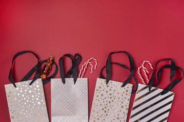 White Gift Shopping Paper Bags with Black Handles Candy Canes and Christmas Toys in Shape of Candy on Red Background Shopping and Holiday Concept Copy Space Top View — Stock Photo, Image