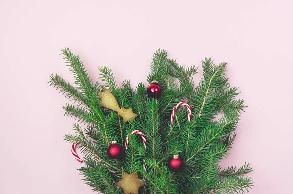 Succursales vertes sapin avec Noël décoré avec des cannes de bonbons de Noël boules rouges et pains d'épices Cookies sur papier rose Vue de dessus Bouquet de Noël horizontal — Photo
