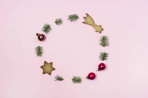 Concept de couronne de Noël Composée de branches de sapin vert Biscuits au pain d'épice et boules de Noël rouges Fond rose des Fêtes Pose horizontale plate — Photo