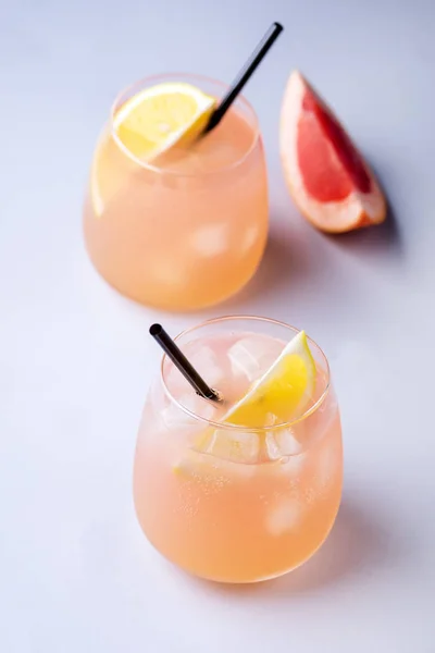 Deux verres de cocktail avec pamplemousse et citron Boisson aux agrumes ou limonade avec glaçons et paille fond bleu vertical — Photo