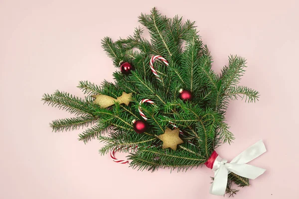 Grüne Zweige Tannenbaum mit Weihnachten dekoriert mit Zuckerstangen rote Kugeln und Lebkuchen auf rosa Papier Hintergrund Draufsicht horizontale Weihnachtsstrauß — Stockfoto