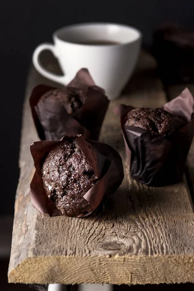 Tre gustosi muffin al cioccolato fatti in casa in carta e tazza bianca di cacao in legno sfondo scuro Foto gustoso dessert — Foto Stock