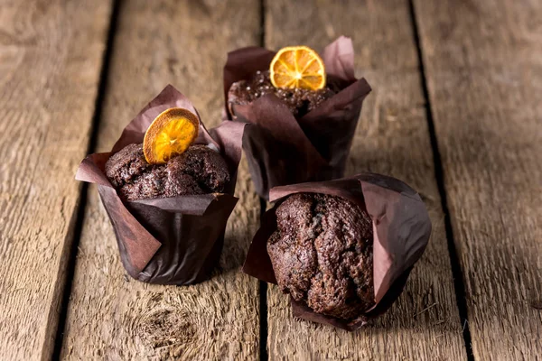 Tre muffin al cioccolato decorati con agrumi secchi su sfondo di legno Dessert fatto in casa orizzontale — Foto Stock