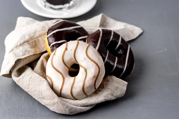 Donuts mit Schokolade und Vanille Sahnehäubchen auf Leinen Serviette auf grauem Hintergrund leckere Dinuts Morgen Frühstückskaffee — Stockfoto