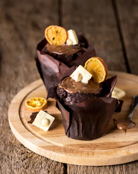 Muffin al cioccolato gustosi fatti in casa decorati con cioccolato bianco e patatine di agrumi su vassoio di legno verticale — Foto Stock