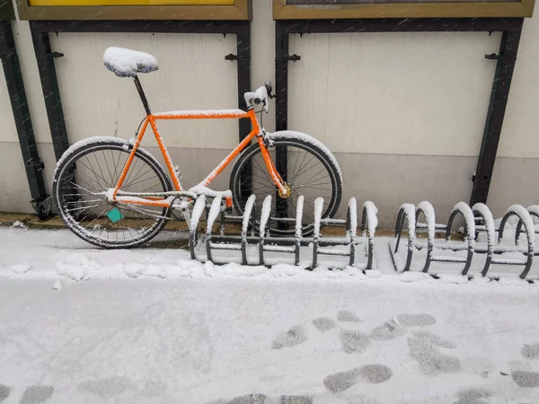 Orange bike locked to a rack. Covered with snow and ice.