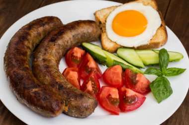 Besleyici kahvaltı Kızarmış sosis, yumurta, kızarmış ekmek, taze salatalık ve domates. Ahşap rustik arka plan. Üstten Görünüm. Yakın çekim