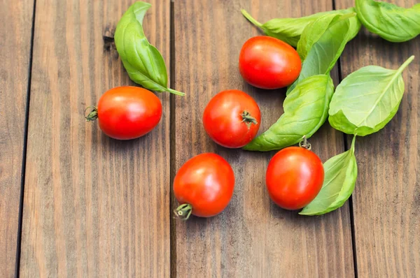 Tomaten mit Basilikumblättern auf einem hölzernen Hintergrund. Ansicht von oben — Stockfoto