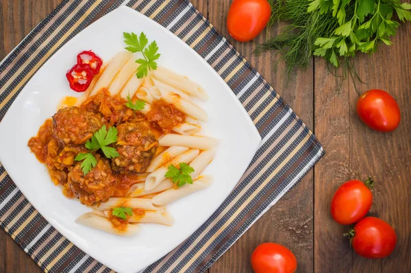 Karbanátky s těstoviny penne v rajčatové omáčce na bílé plotně. Dřevěný rustikální pozadí. Pohled shora. Detail — Stock fotografie