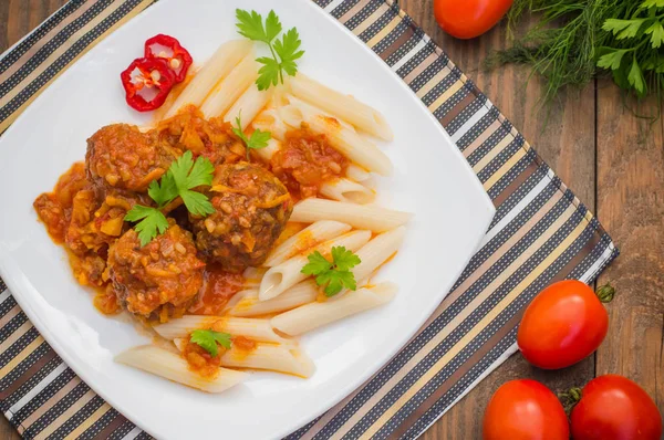 Almôndegas com penne de macarrão em molho de tomate em um prato branco. Fundo rústico de madeira. Vista superior. Close-up — Fotografia de Stock