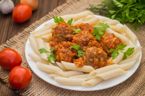 Almôndegas com penne de macarrão em molho de tomate em um prato branco. Fundo rústico de madeira. Vista superior. Close-up — Fotografia de Stock