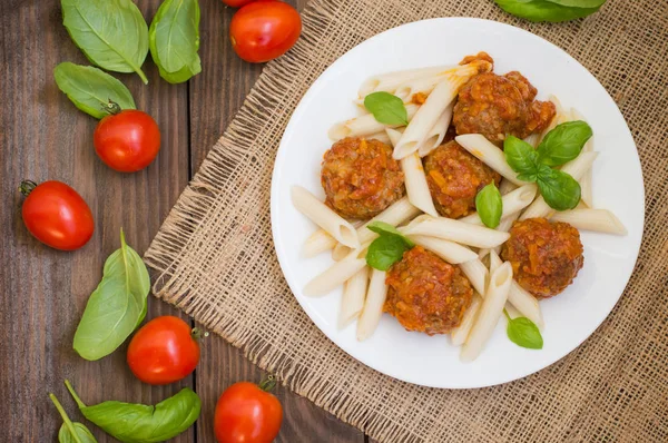 Albóndigas con pasta penne en salsa de tomate en un plato blanco. Fondo rústico de madera. Vista superior. Primer plano —  Fotos de Stock