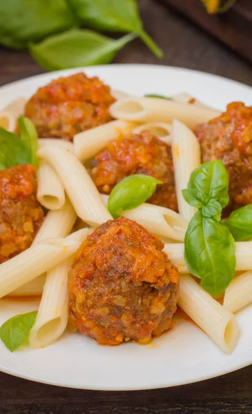 Albóndigas con pasta penne en salsa de tomate en un plato blanco. Fondo rústico de madera. Vista superior. Primer plano —  Fotos de Stock