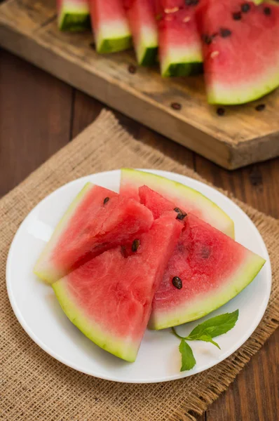 Görögdinnye szeletelve szeleteket a sarj a fa háttér menta. Szemközti nézet — Stock Fotó