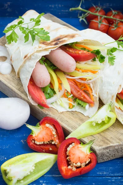 Cachorro quente - sanduíche com linguiça em pita, cenouras coreanas, tomates, cebolas, salsa e pimentão. Fundo de madeira. Fechar. — Fotografia de Stock