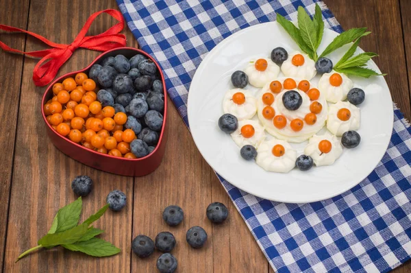 Blueberries and buckthorn laid out in the shape of a heart with cream meringue. Wooden background. Top view. Close-up — Stock Photo, Image