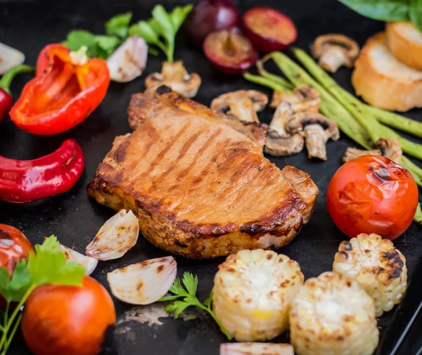 Bistecca sull'osso con verdure cotte alla griglia. Fondo in pietra nera. Vista dall'alto. Focus selettivo primo piano — Foto Stock