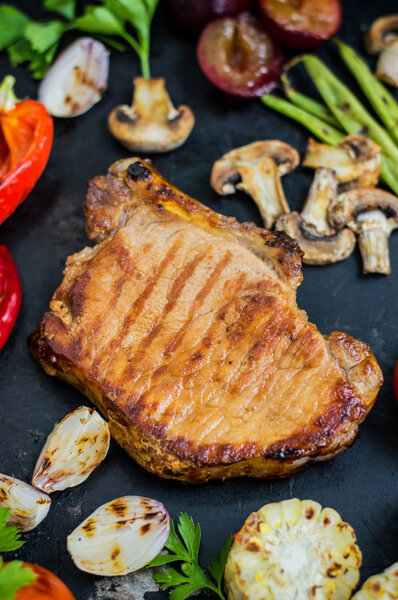 Steak on the bone with vegetables cooked  the grill. Black stone background. Top view. Selective focus close-up