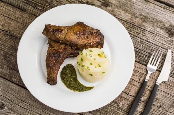 Pork steak op het bot gegrild met geprakte aardappelen en spinazie kruiden saus. Houten achtergrond. Close-up. Bovenaanzicht — Stockfoto