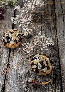 Profiterol çikolatada sırlı ve ceviz talaşı ile serpilir. Ahşap arka plan. Yakın çekim