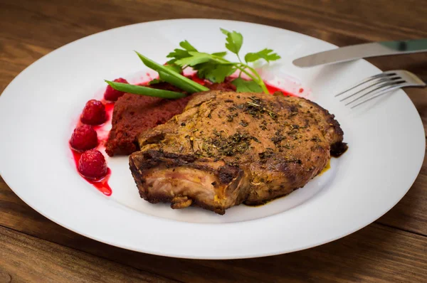 Gebratenes Schweinesteak auf Knochen mit Gemüse, Rote-Bete-Püree und Beerensauce. Holzuntergrund. Ansicht von oben. Nahaufnahme — Stockfoto