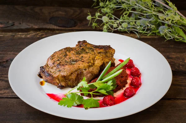 Bifteck de porc grillé sur l'os avec des légumes, de la purée de betterave et de la sauce aux baies. Fond en bois. Vue de dessus. Gros plan — Photo