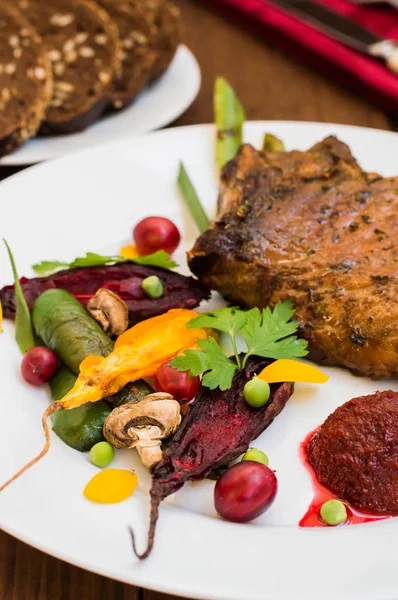 Gebratenes Schweinesteak auf Knochen mit Gemüse, Rote-Bete-Püree und Beerensauce. Holzuntergrund. Ansicht von oben. Nahaufnahme — Stockfoto