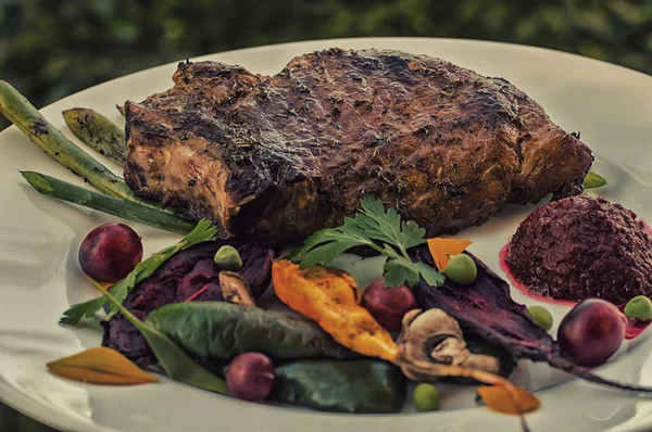 Gebratenes Schweinesteak auf Knochen mit Gemüse, Rote-Bete-Püree und Beerensauce. vor dem Hintergrund von Laub. Nahaufnahme — Stockfoto