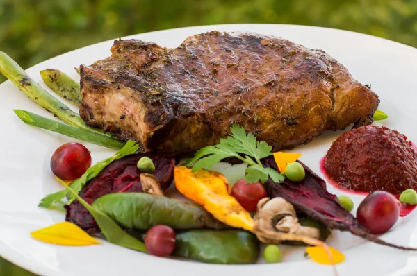 Stekt grillad Fläskstek med ben med grönsaker, mosade rödbetor och bärsås. Mot bakgrund av bladverk. Närbild — Stockfoto