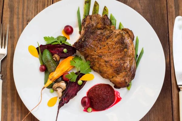 Stekt grillad Fläskstek med ben med grönsaker, mosade rödbetor och bärsås. Trä bakgrund. Ovanifrån. Närbild — Stockfoto