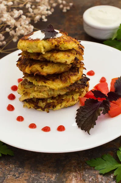 Zucchini Pancakes with sour cream, tomatoes and herbs. Old background. Close-up