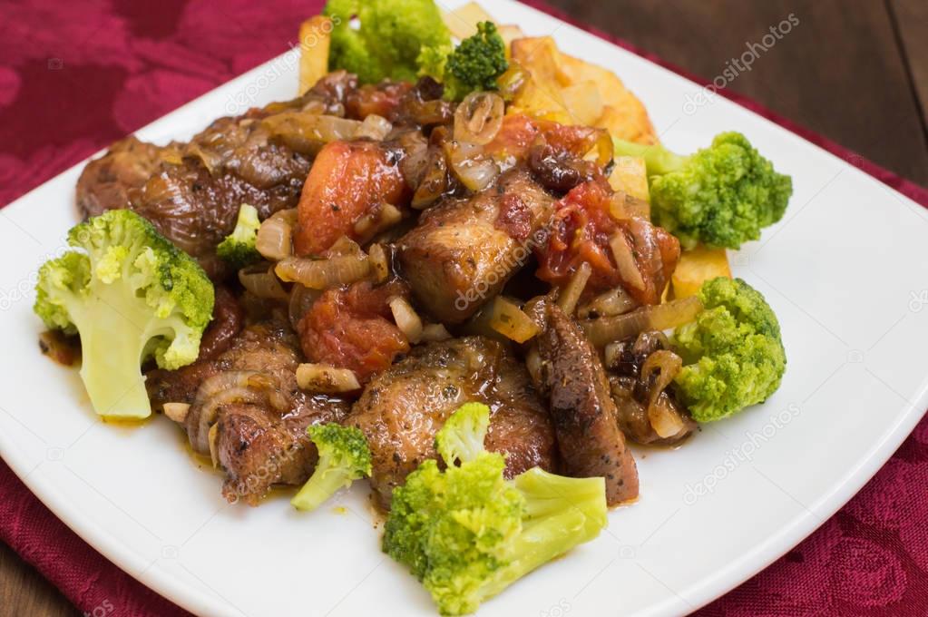 Stifado - a traditional Cypriot dishes, spread in Greece. It consists of  stew with tomatoes, potatoes, broccoli, onions, garlic and spicy spices. Wooden rustic table. Top view. Close-up