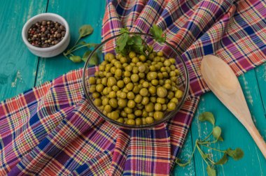 Ahşap masa üstten görünüm kaşık ile şeffaf bir tabak içinde konserve bezelye