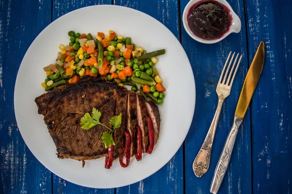 Grilovaný steak s dušenou zeleninou na bílé plotně. modrá tabulka. Pohled shora — Stock fotografie