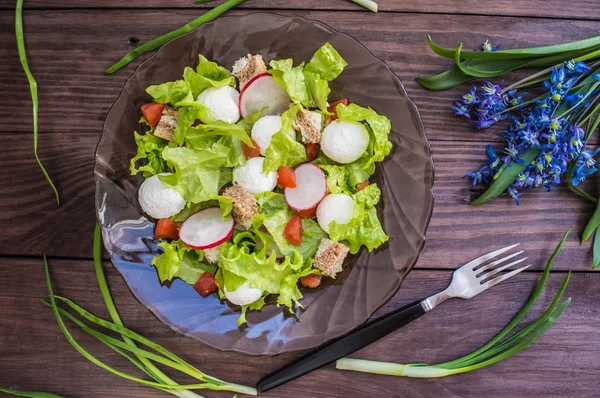 Salade de laitue, radis, craquelins, tomates et fromage sur une assiette circassienne noire transparente. Table en bois — Photo