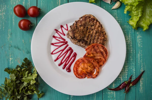 Steak panggang dengan sayuran dan saus berry di piring putih. Latar belakang kayu pirus. Tampilan atas — Stok Foto