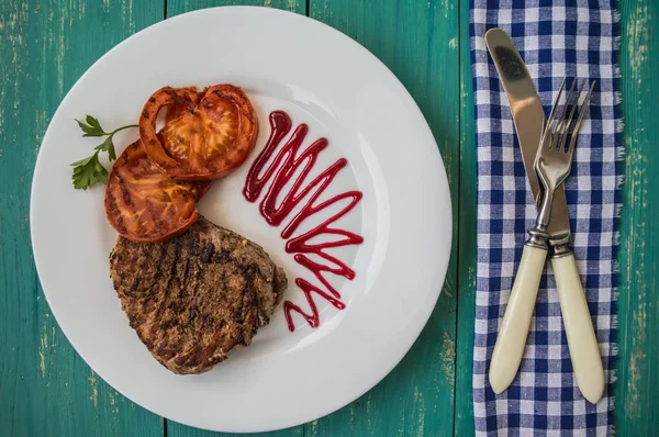 Filete a la parrilla con verduras y salsa de bayas en un plato blanco. Fondo de madera turquesa. Vista superior —  Fotos de Stock