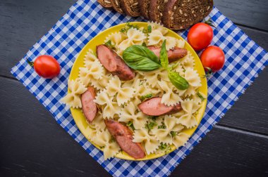 Makarna, ekmek, otlar ve kiraz domates dilimleri ile ızgara sosis dilim dilimlenmiş. Üstten Görünüm. ahşap siyah arka plan... . Yakın çekim