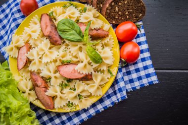 Makarna, ekmek, otlar ve kiraz domates dilimleri ile ızgara sosis dilim dilimlenmiş. Üstten Görünüm. ahşap siyah arka plan... . Yakın çekim