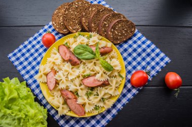 Makarna, ekmek, otlar ve kiraz domates dilimleri ile ızgara sosis dilim dilimlenmiş. Üstten Görünüm. ahşap siyah arka plan... . Yakın çekim