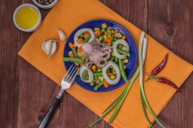 Ahtapot ve kalamar halkaları üzerinde taze sebze mavi plaka ahşap arka plan. Üstten Görünüm. Yakın çekim