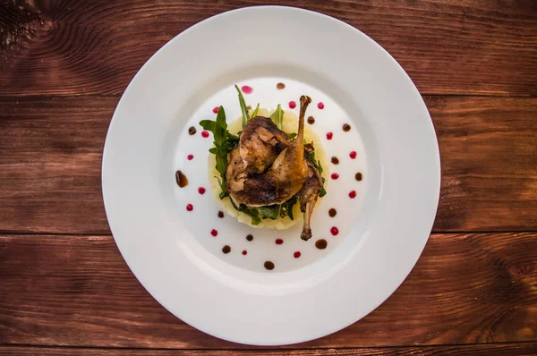 Caille rôtie sur un lit avec purée de pommes de terre, feuilles de fusée et sauce aux baies. plaque blanche fond rustique en bois. Vue de dessus. Gros plan — Photo