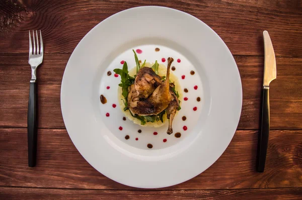 Caille rôtie sur un lit avec purée de pommes de terre, feuilles de fusée et sauce aux baies. plaque blanche fond rustique en bois. Vue de dessus. Gros plan — Photo