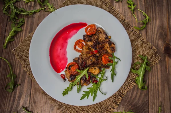 Plat de viande rôtie sur le gril avec sauce aux baies et roquette dans le restaurant. Fond rustique en bois. Vue de dessus. Gros plan — Photo