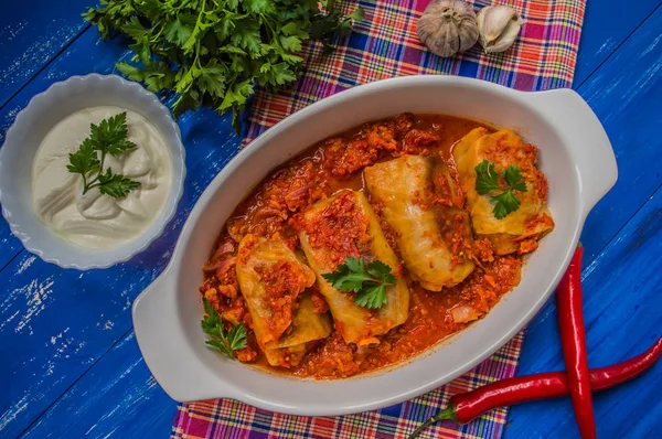 Cena con involtini di cavolo in salsa di pomodoro decorata con prezzemolo. Sfondo rustico blu legno. Vista dall'alto. Primo piano — Foto Stock