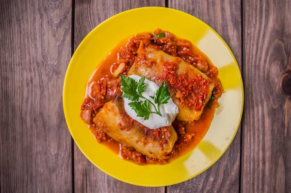 Cena con involtini di cavolo in salsa di pomodoro decorata con prezzemolo. Sfondo rustico in legno. Vista dall'alto. Primo piano — Foto Stock