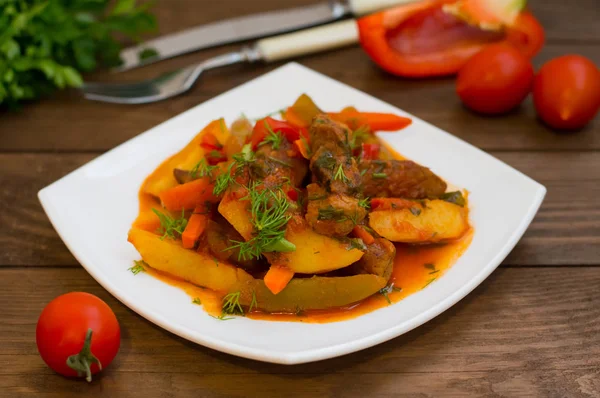 Guiso con papas, zanahorias, encurtidos, tomates y pimientos picantes. Azu de Tartarian en una placa cuadrada blanca. Fondo rústico de madera. Vista superior. Primer plano —  Fotos de Stock