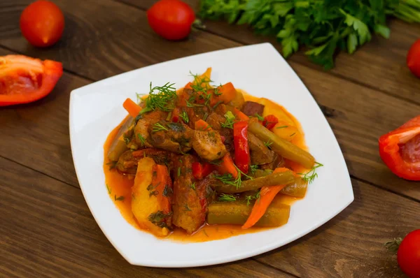 Stufato con patate, carote, sottaceti, pomodori e peperoncini. Azu di tartaro su un piatto quadrato bianco. Sfondo rustico in legno. Vista dall'alto. Primo piano — Foto Stock